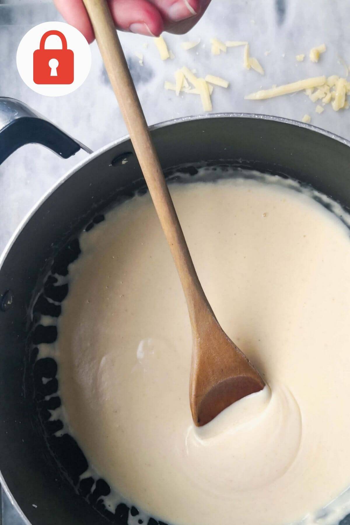 Cheesy bechamel sauce in a pot with a wooden spoon.