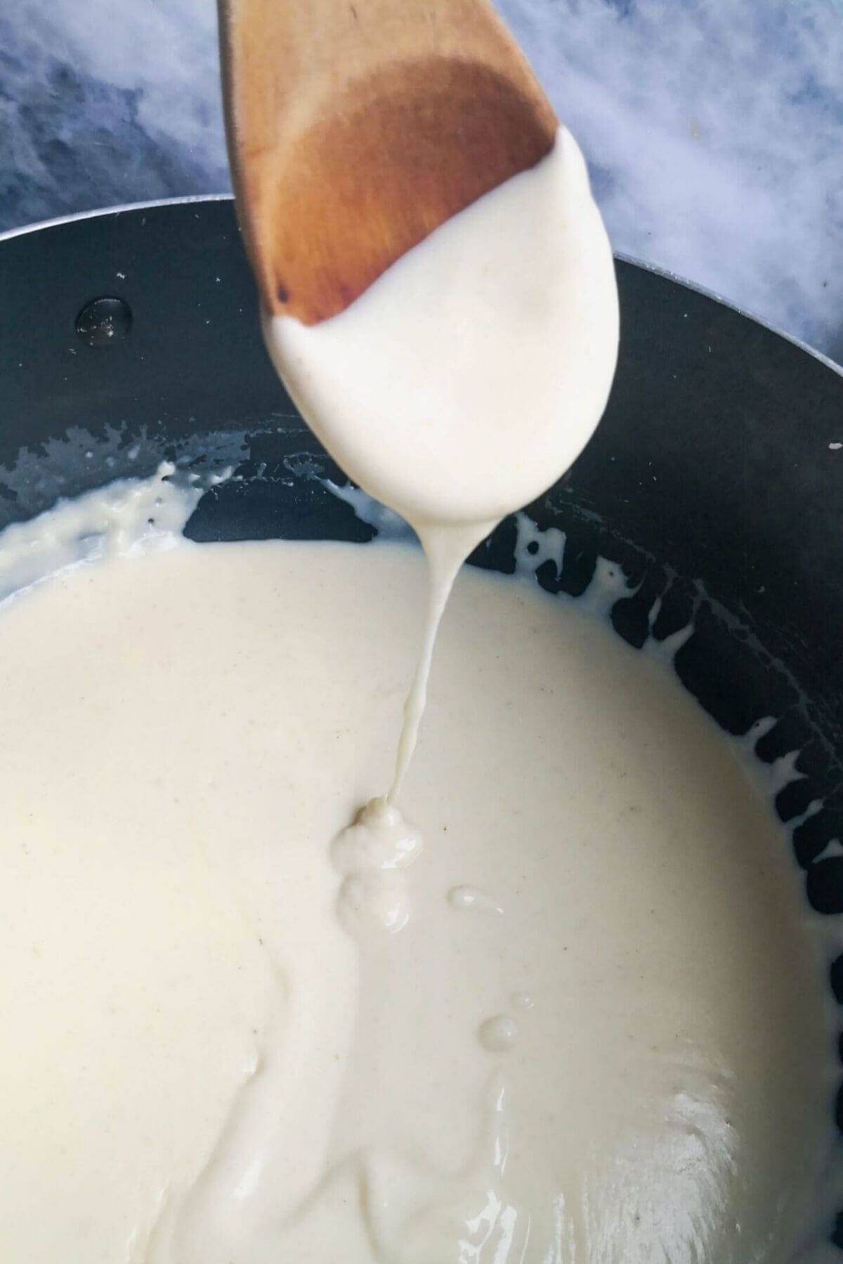 Cheesy bechame sauce on wooden spoon over a pot.