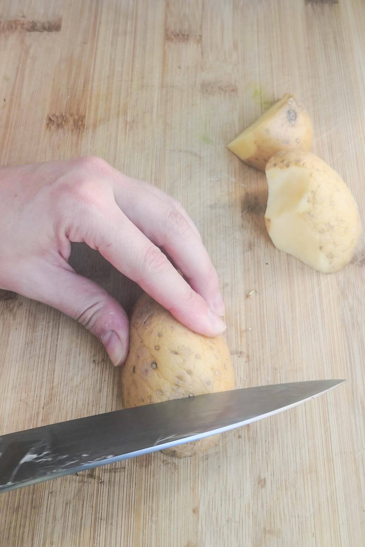 Chopping potatoes into chunky wedges on a wooden board.