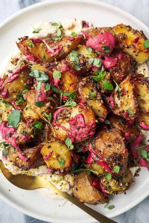 Crispy dukkah potatoes on a bed of aioli with thyme and pink tahini scattered on top.