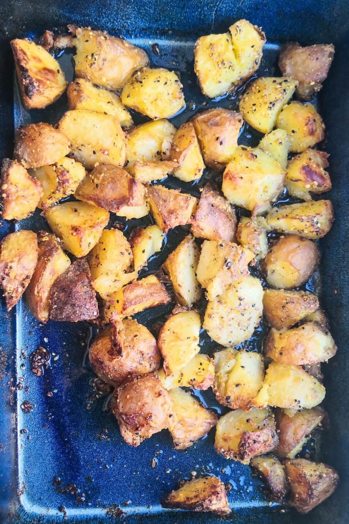 Crispy dukkah potatoes after roasting in a large blue oven dish.