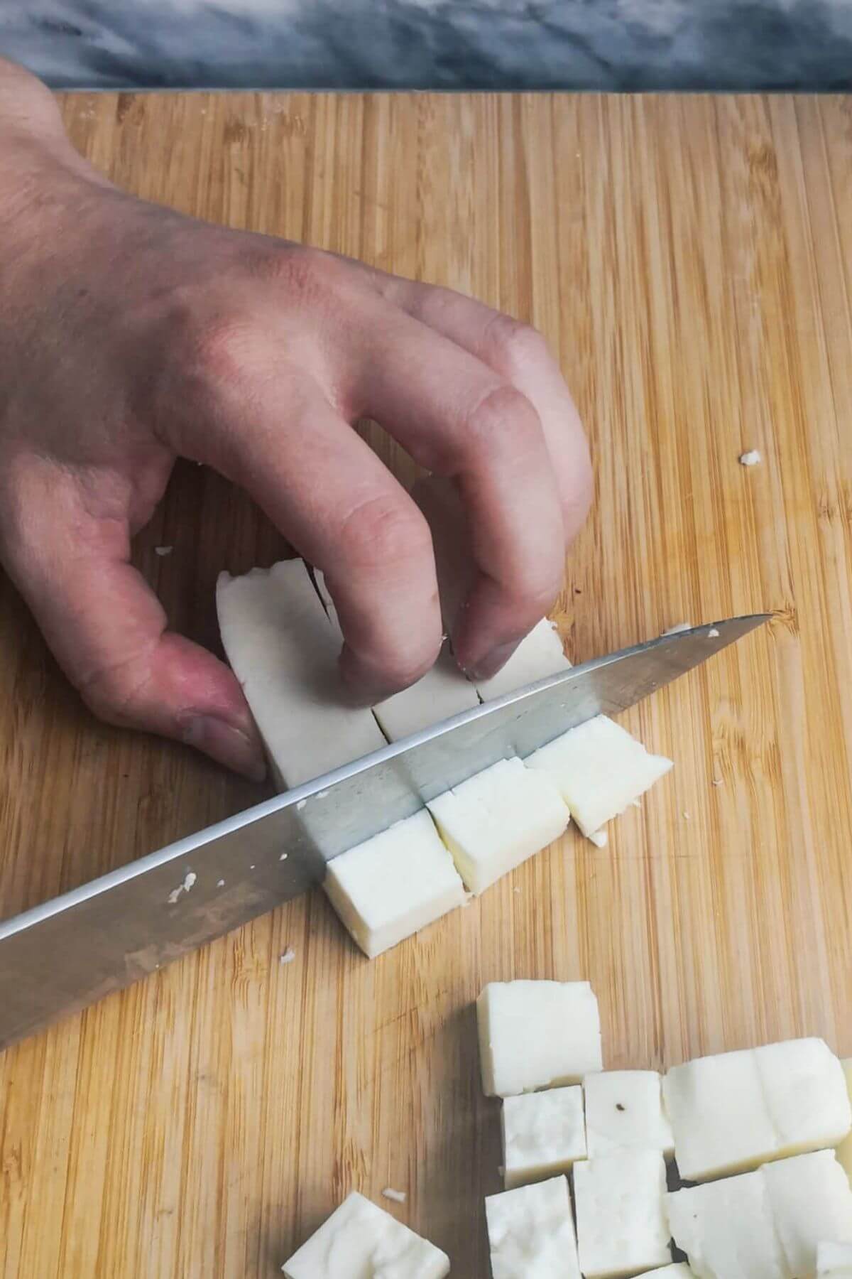 Chopping halloumi into squares on a wooden board.