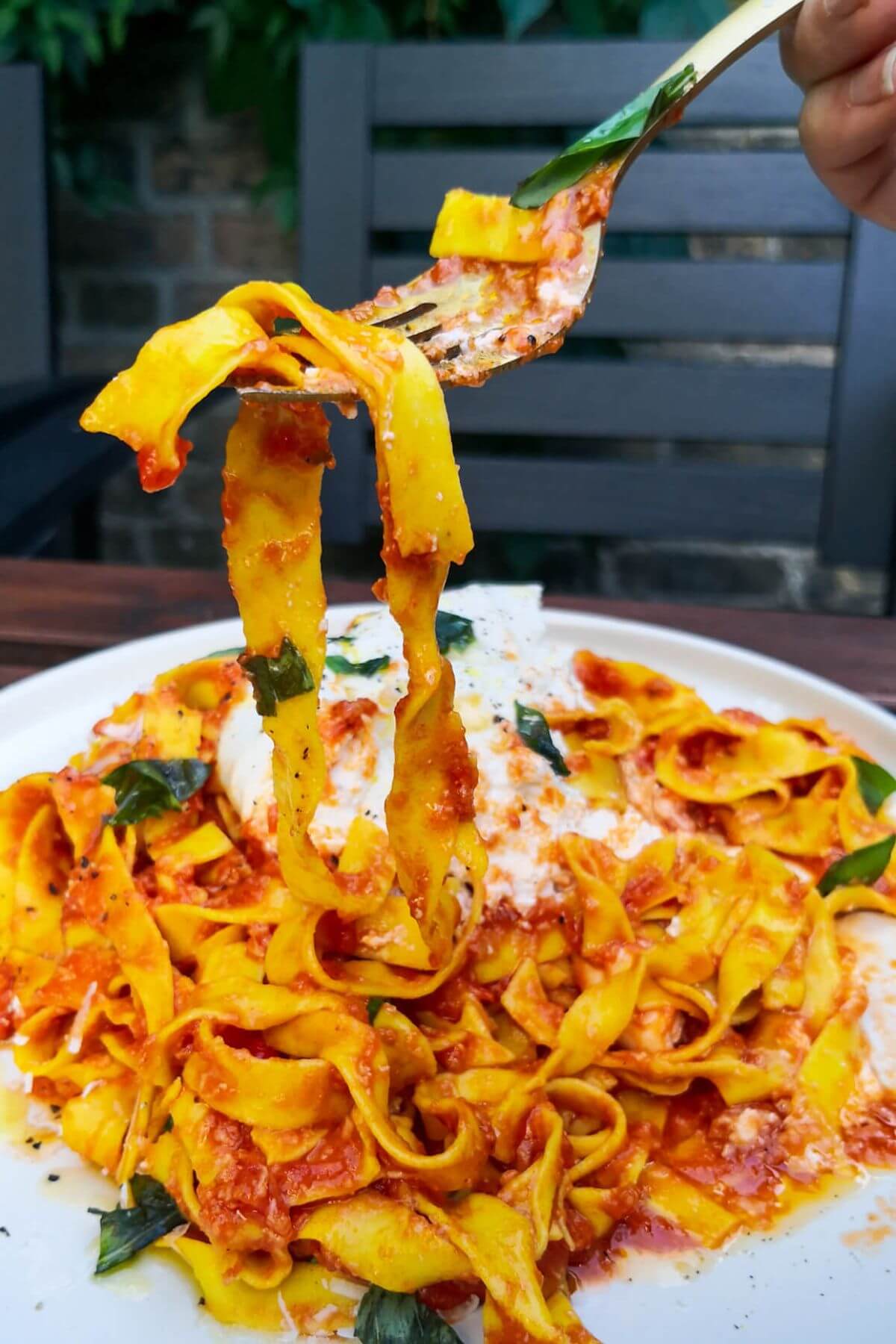 Nduja pasta being pulled up by a fork from a large whie plate of pasta.
