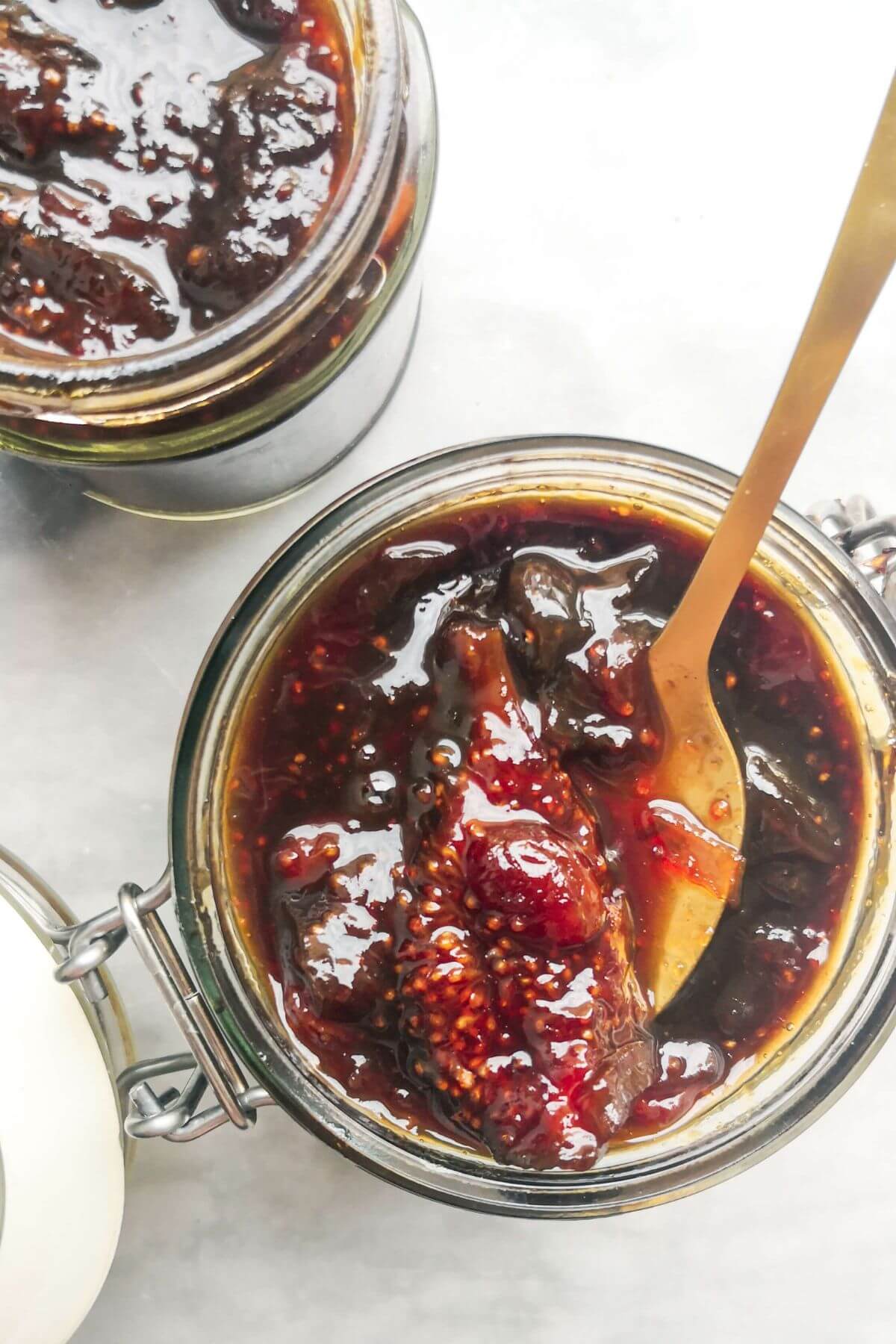 Fig chutney in a glass jar with a gold spoon inside.