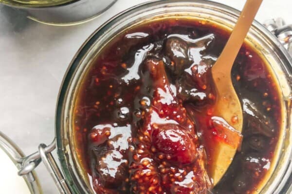 Fig chutney in a glass jar with a gold spoon inside.