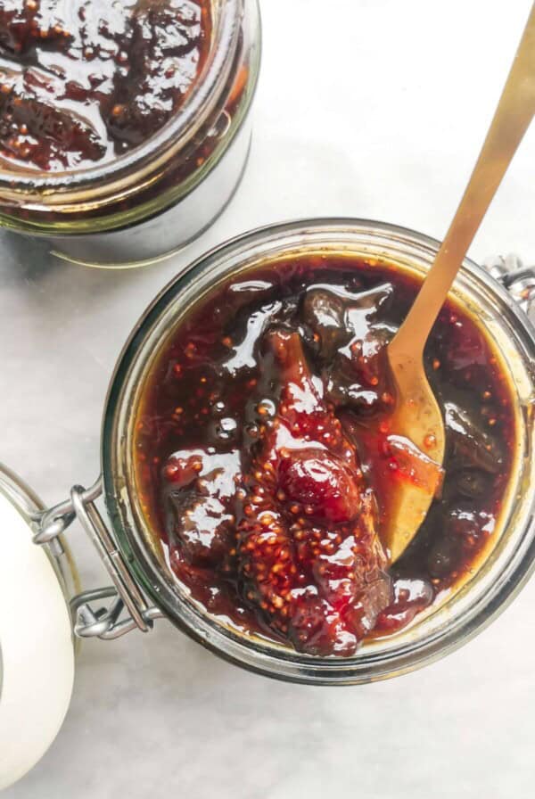 Fig chutney in a glass jar with a gold spoon inside.
