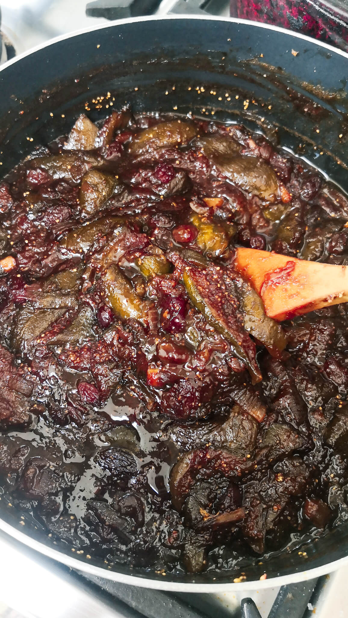 A large wooden spoon stirring fig chutney in a large pot.