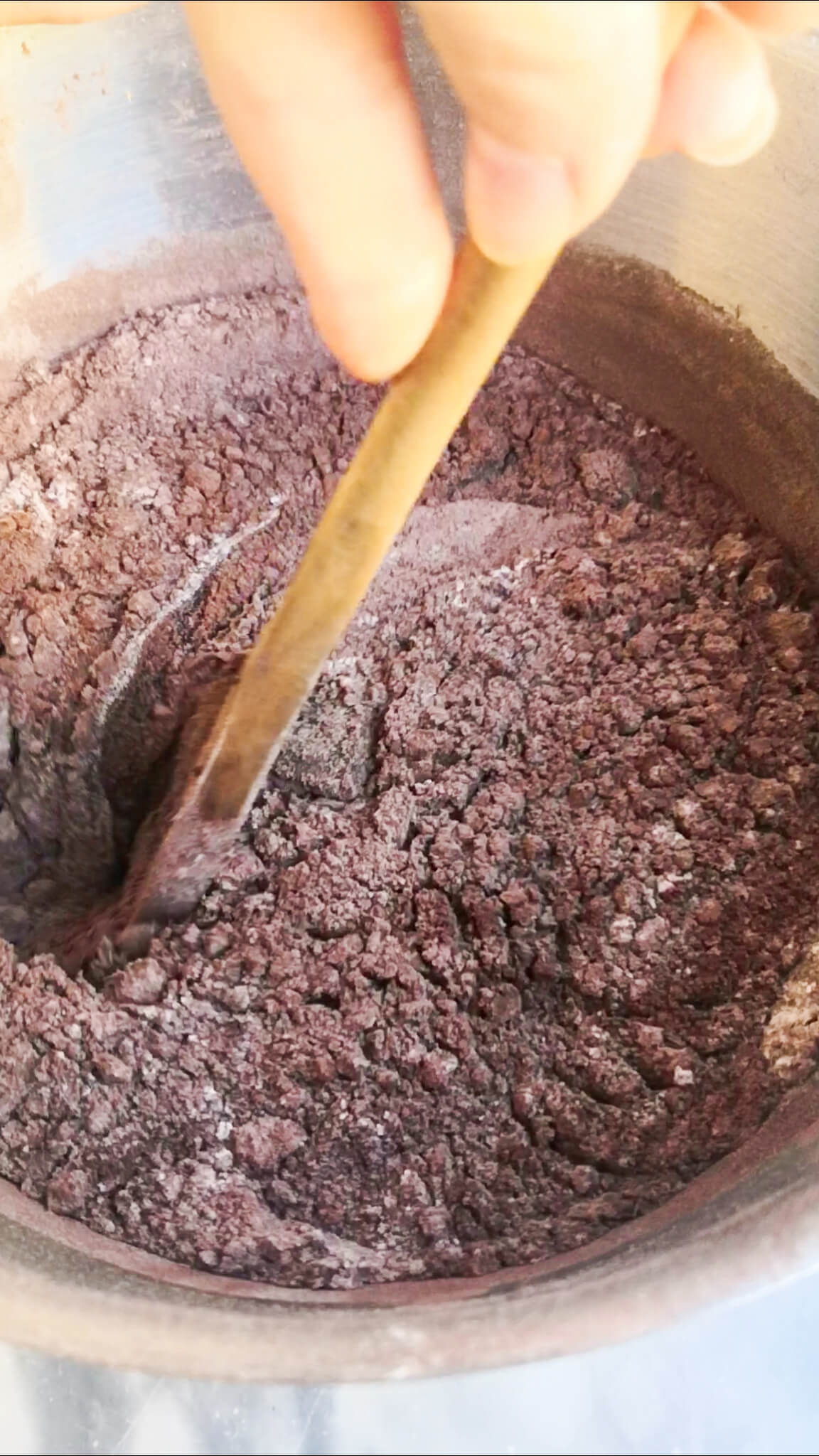 Wooden spoon mixing cocoa powder and flour into eggs, sugar and butter mix.