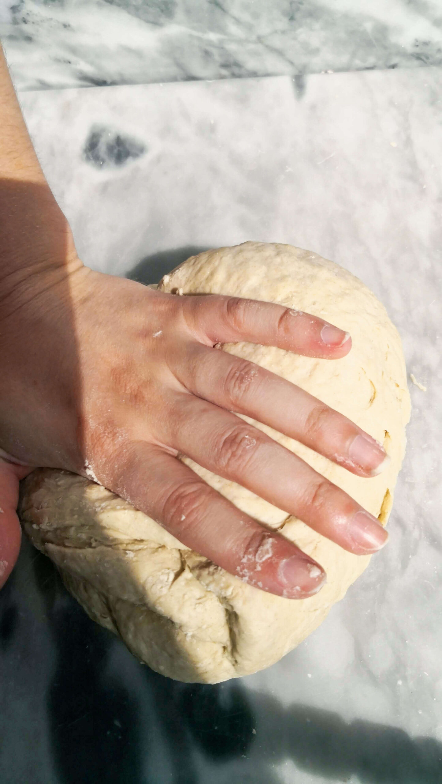 Hand folding over a ball of dough on a grey marble surface.