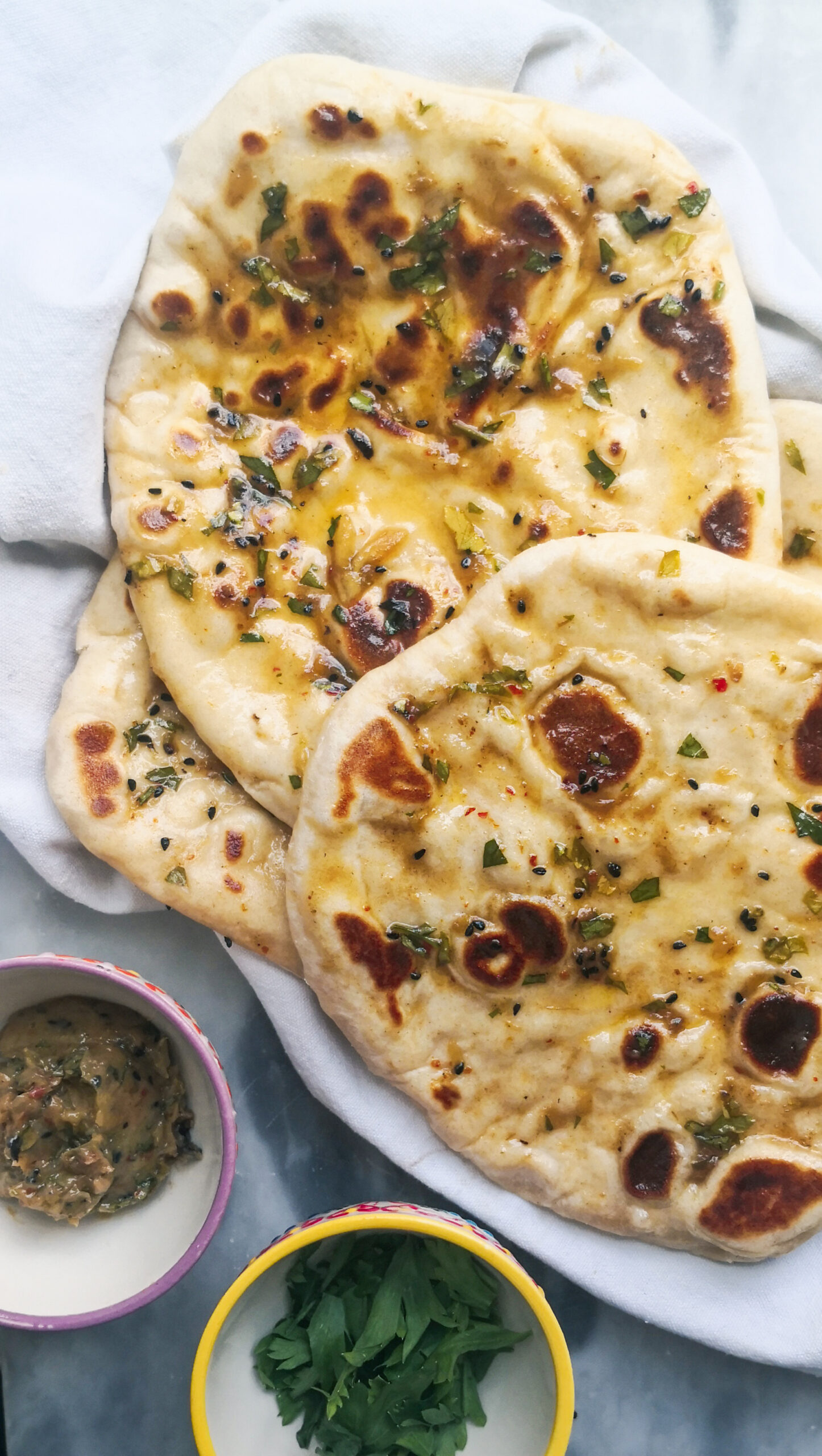 Garlic flatbreads on a white tea towel with garlic butter and parsley on the side.