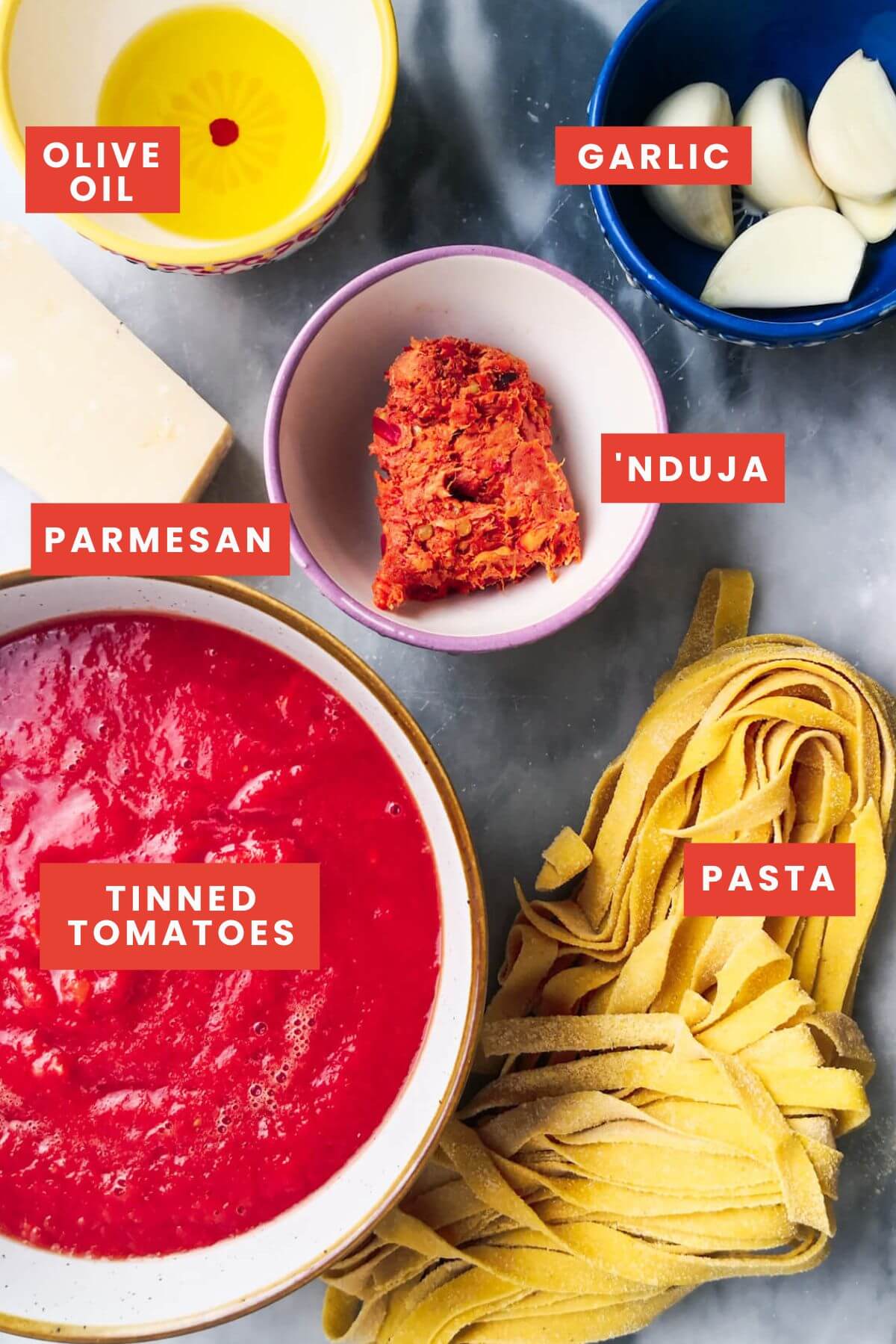 Ingredients for nduja pasta laid out on a grey marble background and labelled.