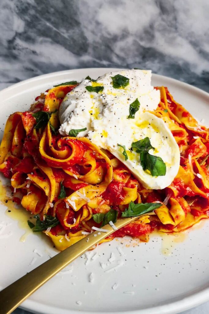 Spicy nduja pasta on a white plate with a ball of burrata on top.