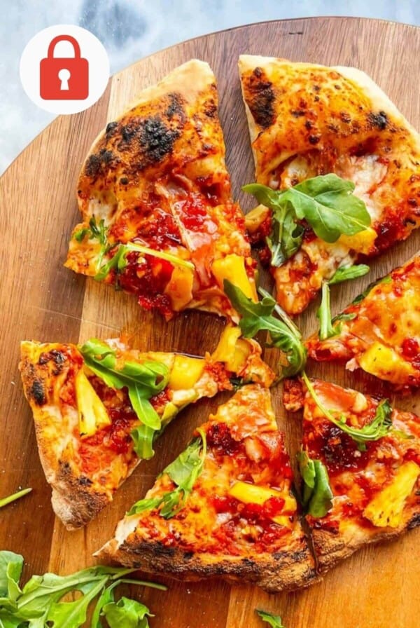 Spicy Hawaiian pizza with rocket on top sliced, sitting on a wooden board.