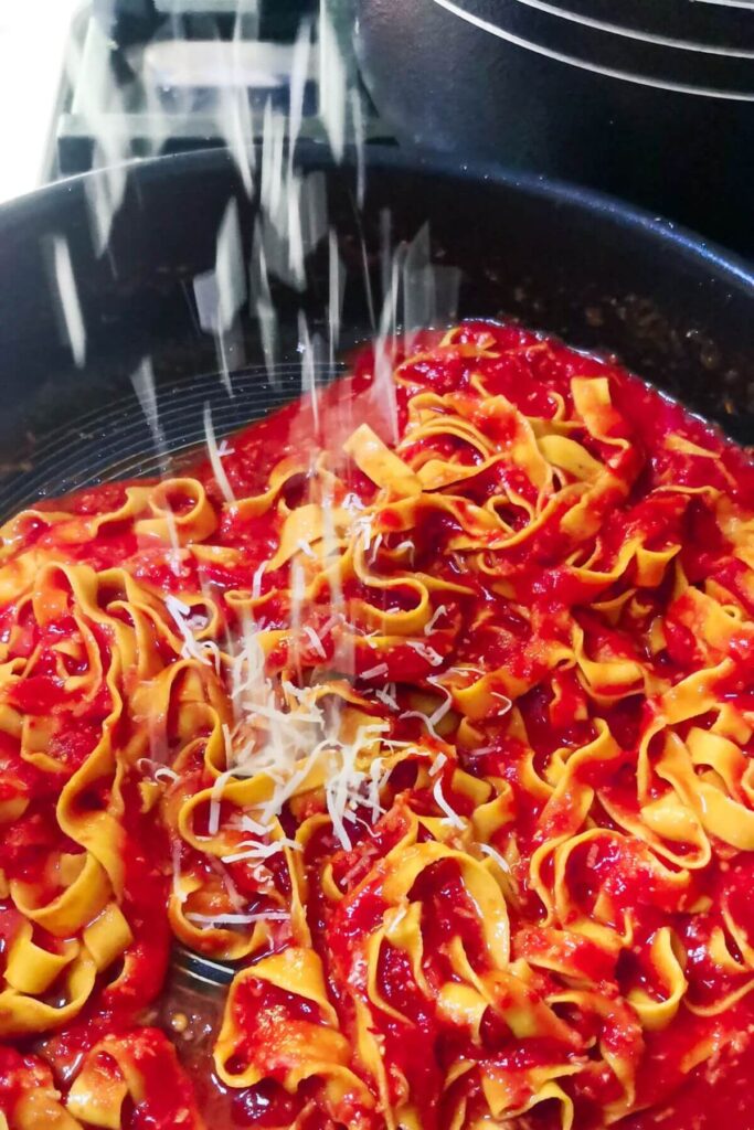 Grated parmesan being scattered on top of nduja pasta in a large pan.