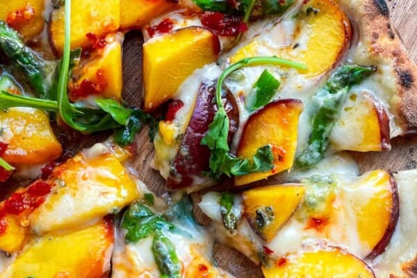 Peach blue cheese pizza sliced on a wooden board.