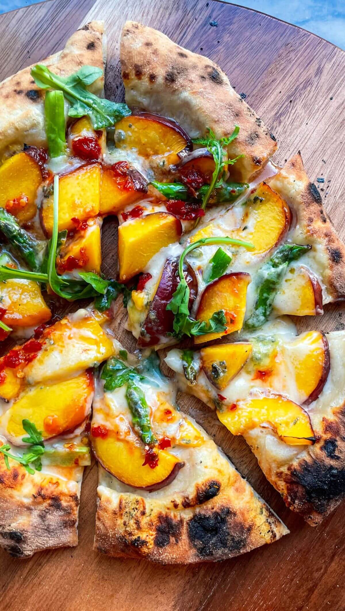 Peach blue cheese pizza sliced on a wooden board.