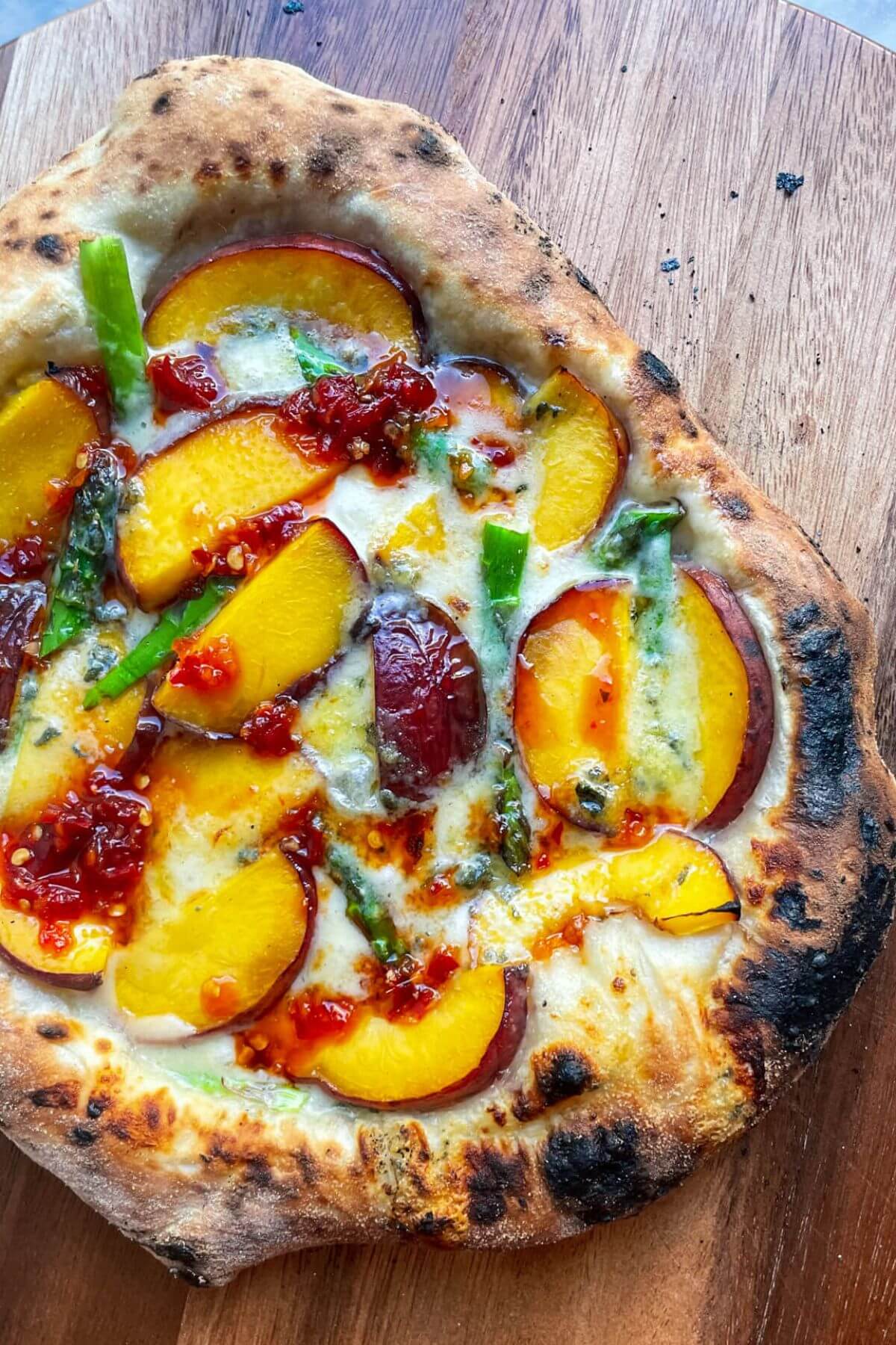 Peach, asparagus, blue cheese pizza with chilli jam drizzle on a wooden board.