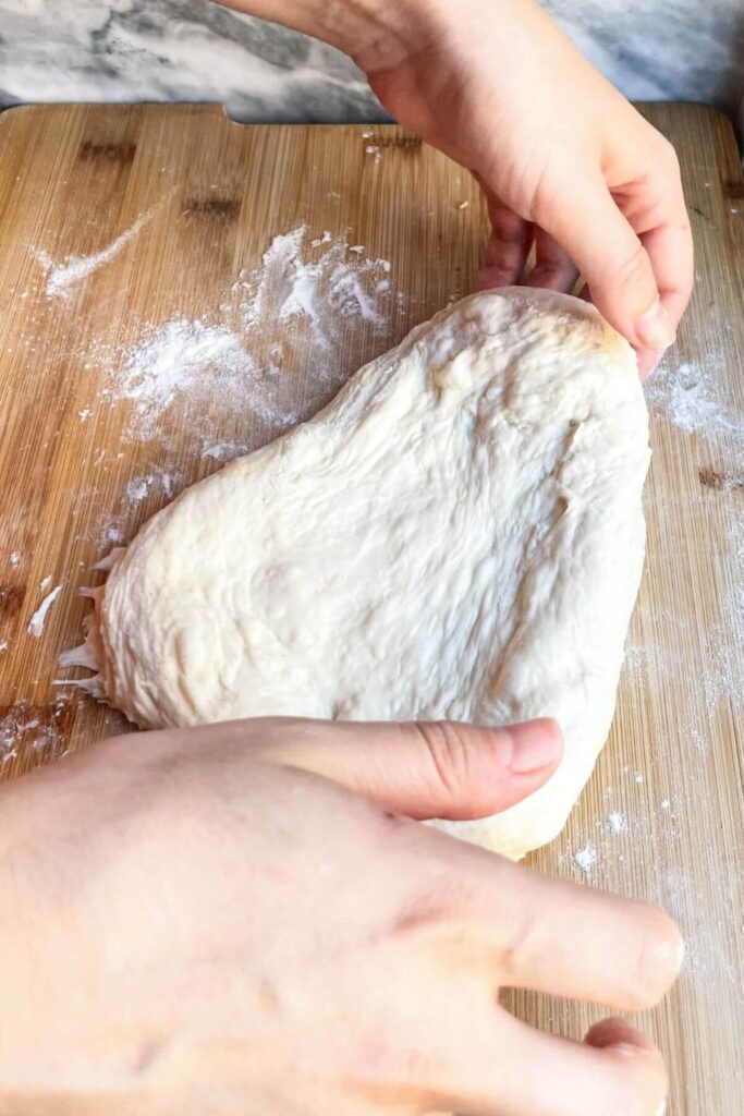 Hands pulling dough out to form a pizza base.