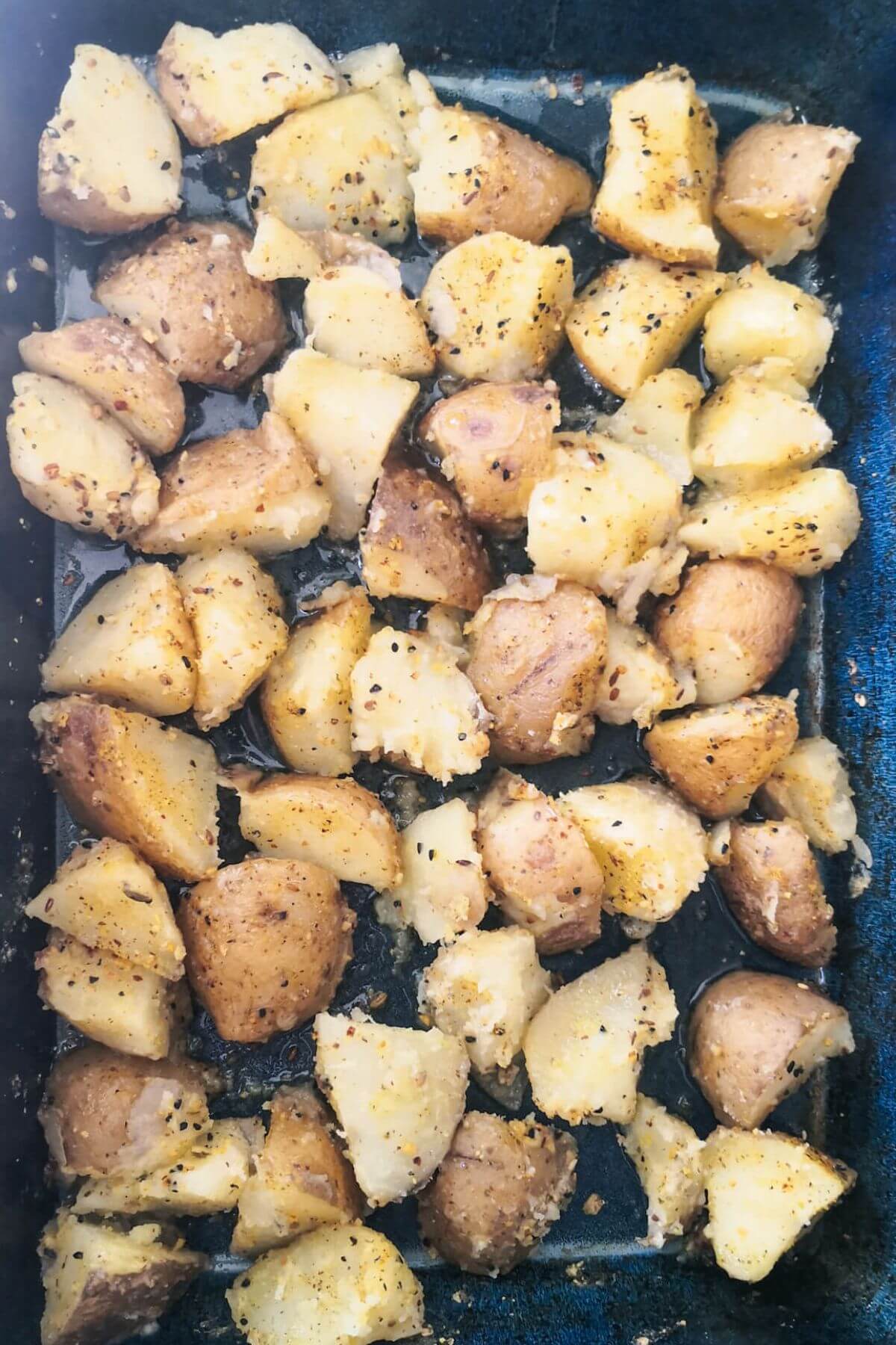 Dukkah potatoes in a large blue oven dish ready to go into the oven.