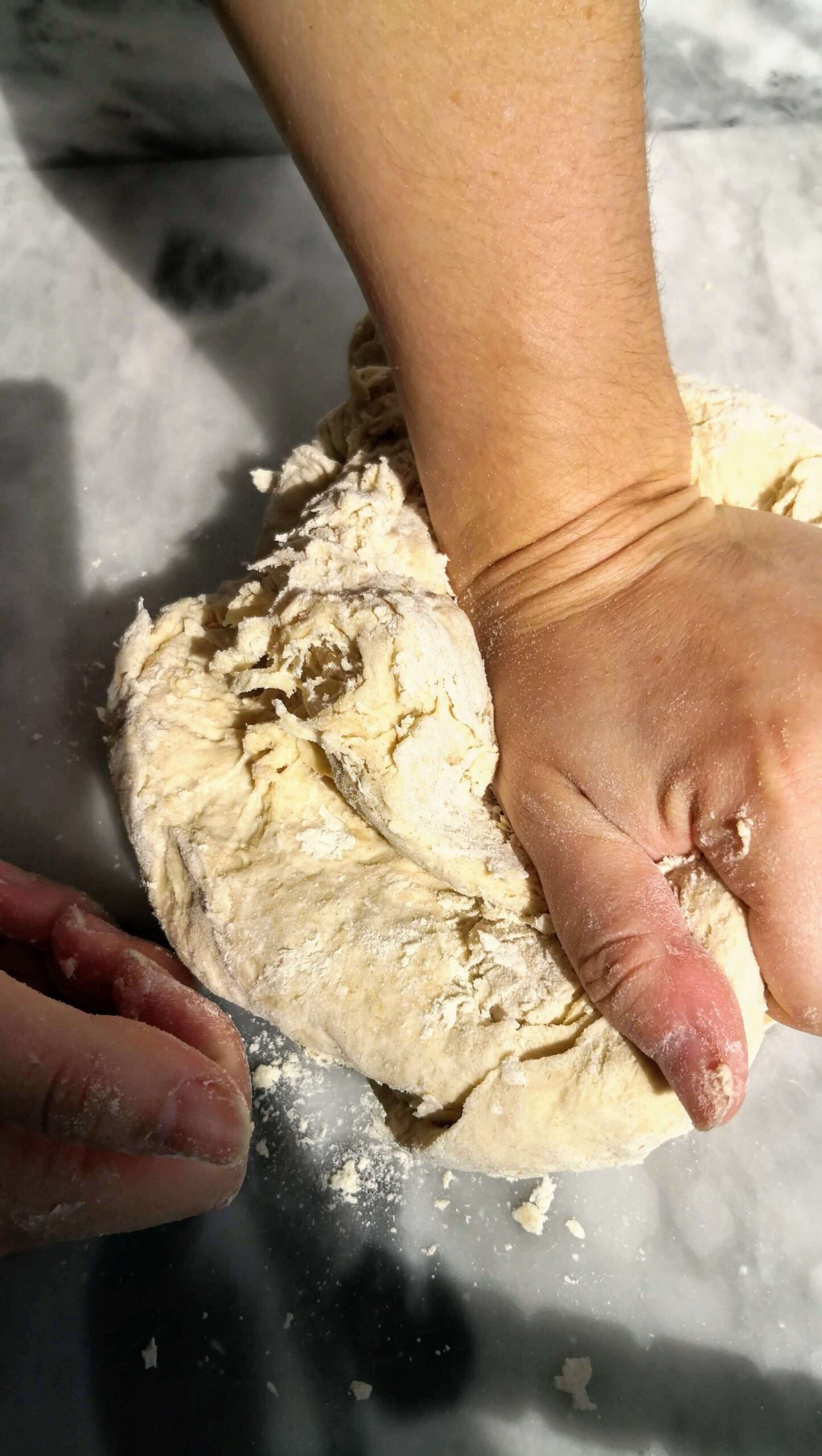 Hand pressing down on dough on a grey marble surface.