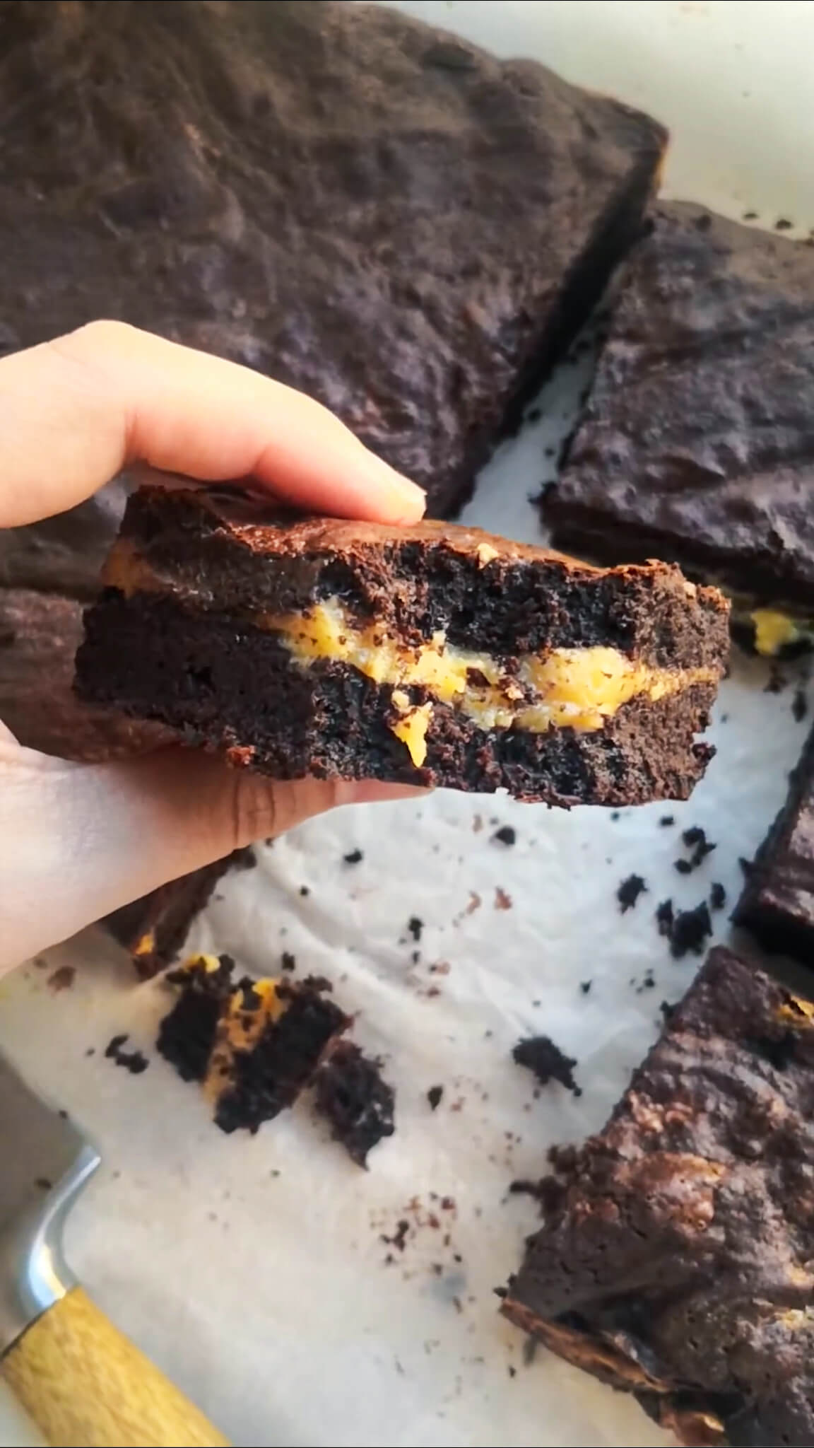 Hand holding up a salted caramel brownie with more brownies in the background.