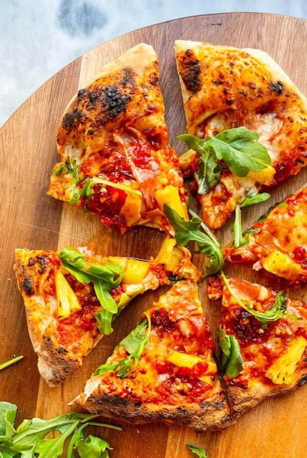 Spicy Hawaiian pizza with rocket on top sliced, sitting on a wooden board.
