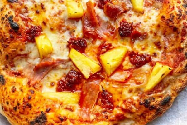 Spicy Hawaiian pizza on baking paper on a round wooden board.