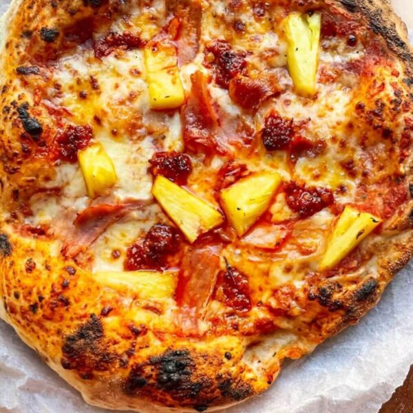 Spicy Hawaiian pizza on baking paper on a round wooden board.