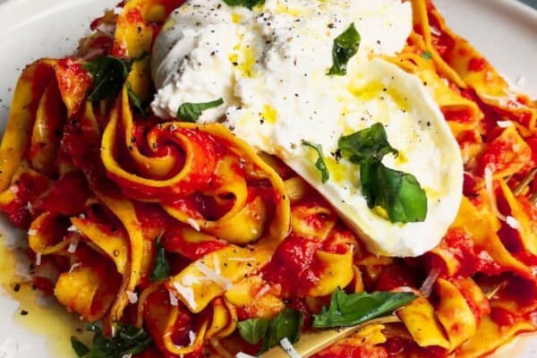 Close up view of spicy nduja pasta on a white plate with a gold fork on a grey marble background.