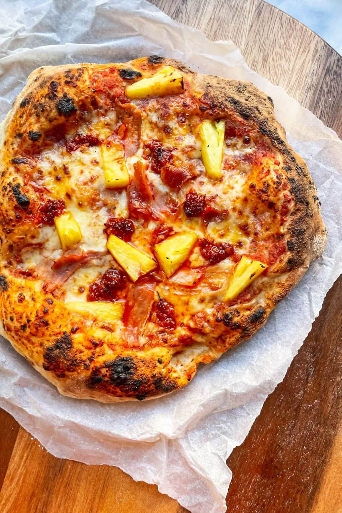 Spicy Hawaiian pizza on baking paper on a round wooden board.