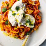 Spicy nduja pasta with torn burrata ball on top with basil on a white plate with a gold fork.