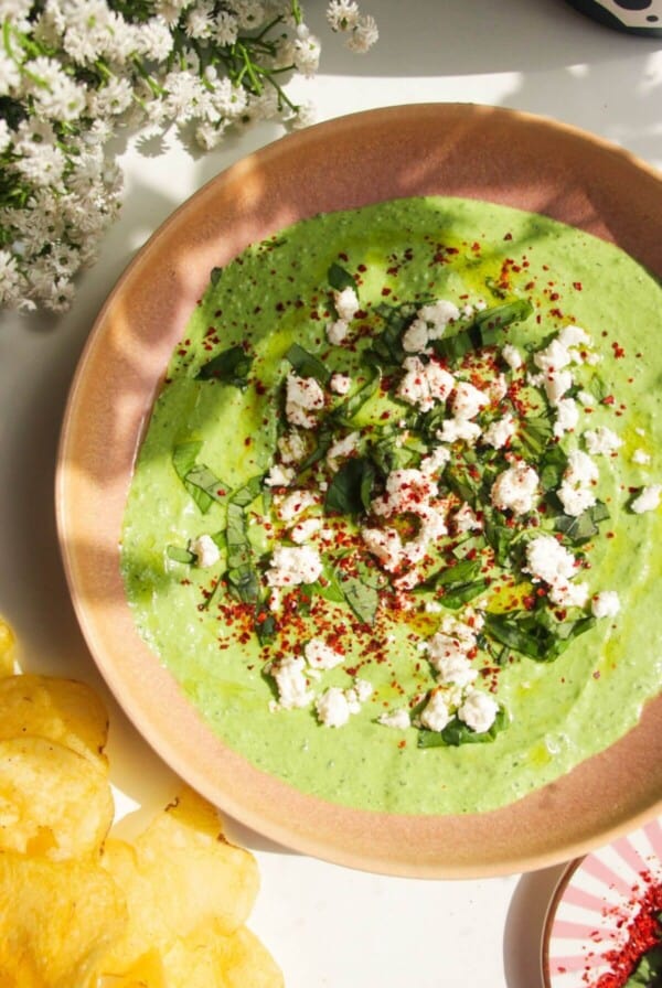 Spinach and feta dip in a pink bowl with chips on the side.
