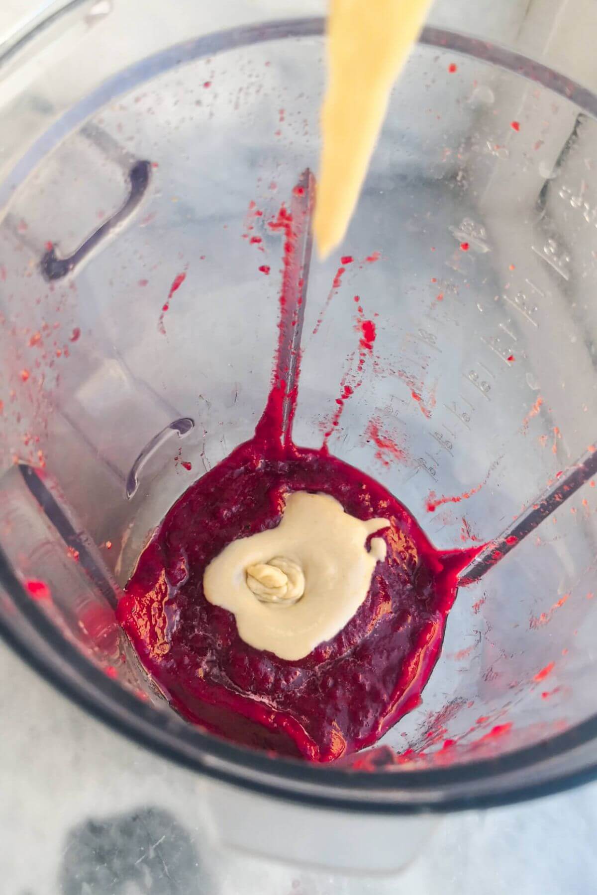 Tahini being added to a blender with beetroot puree.