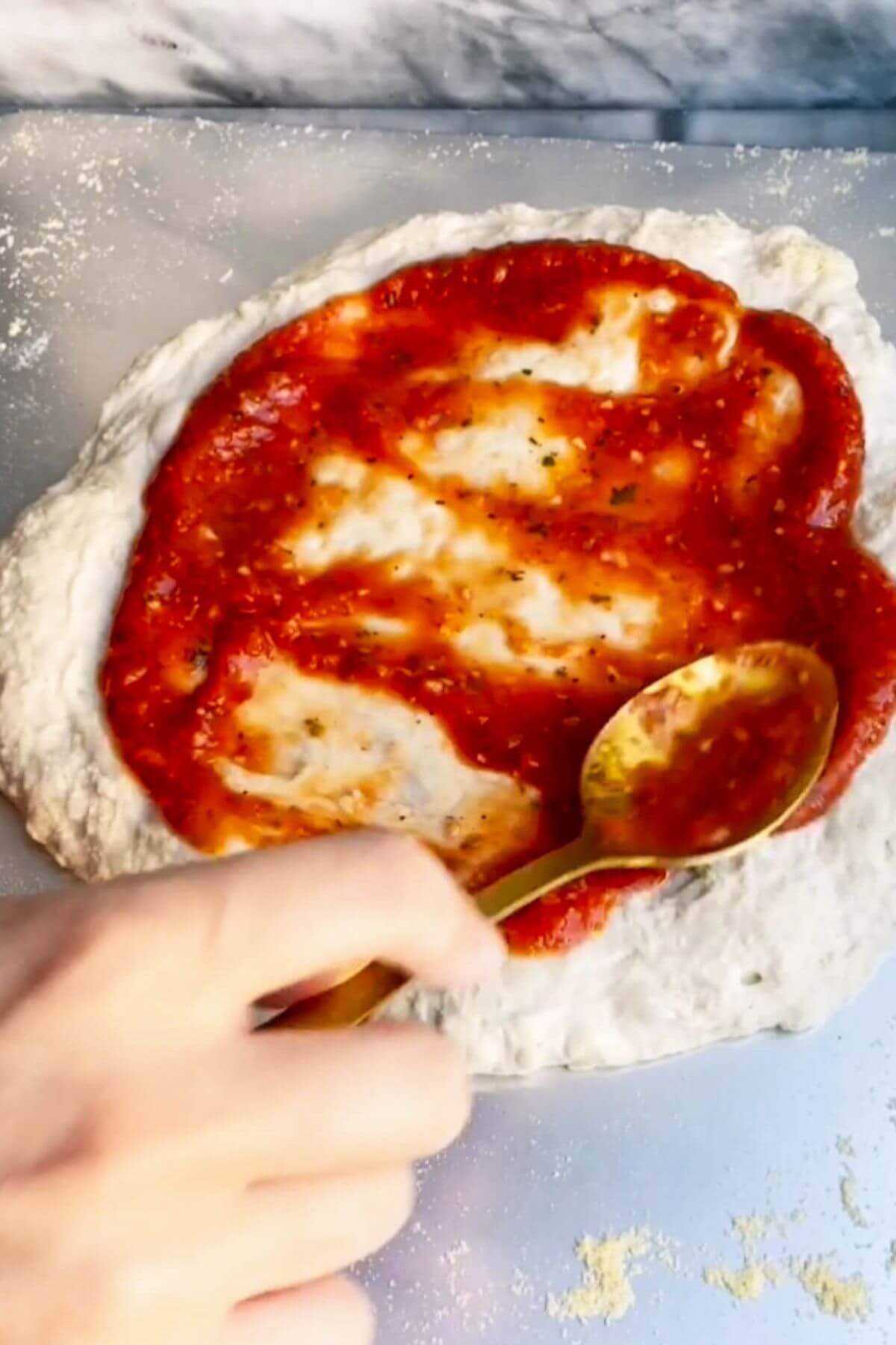 Spooning red pizza sauce onto pizza base.