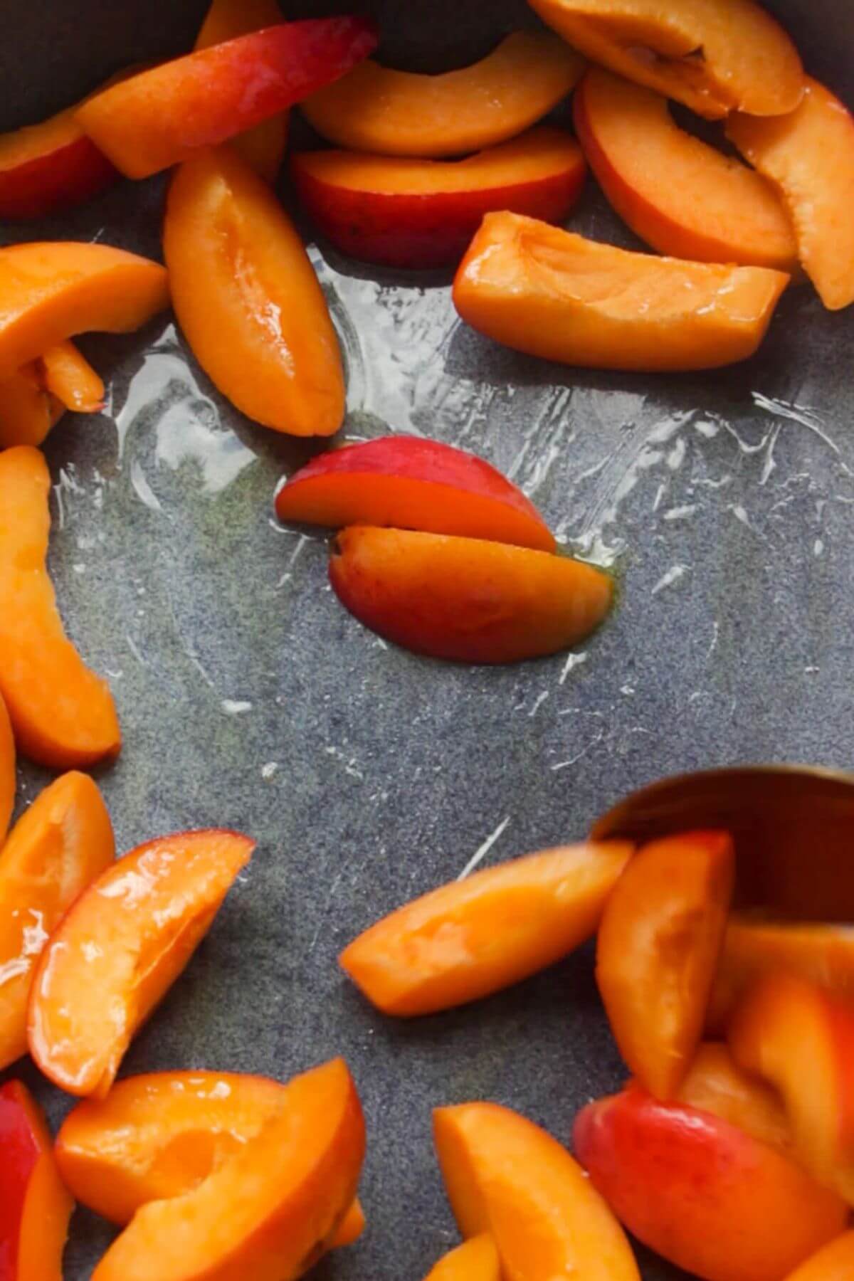 Spoon stirring olive oil through sliced apricots in a small blue oven dish.