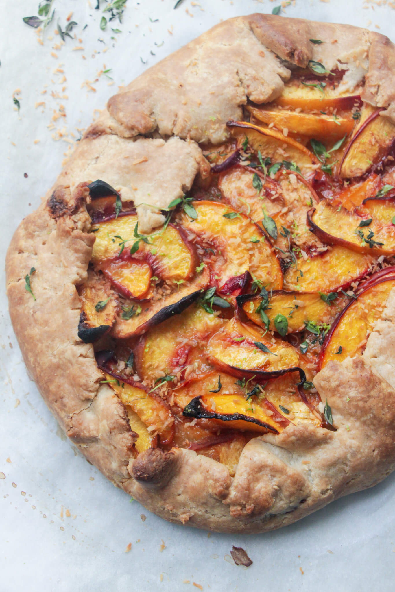 Peach almond galette with thyme leaves close up on a piece of baking paper.