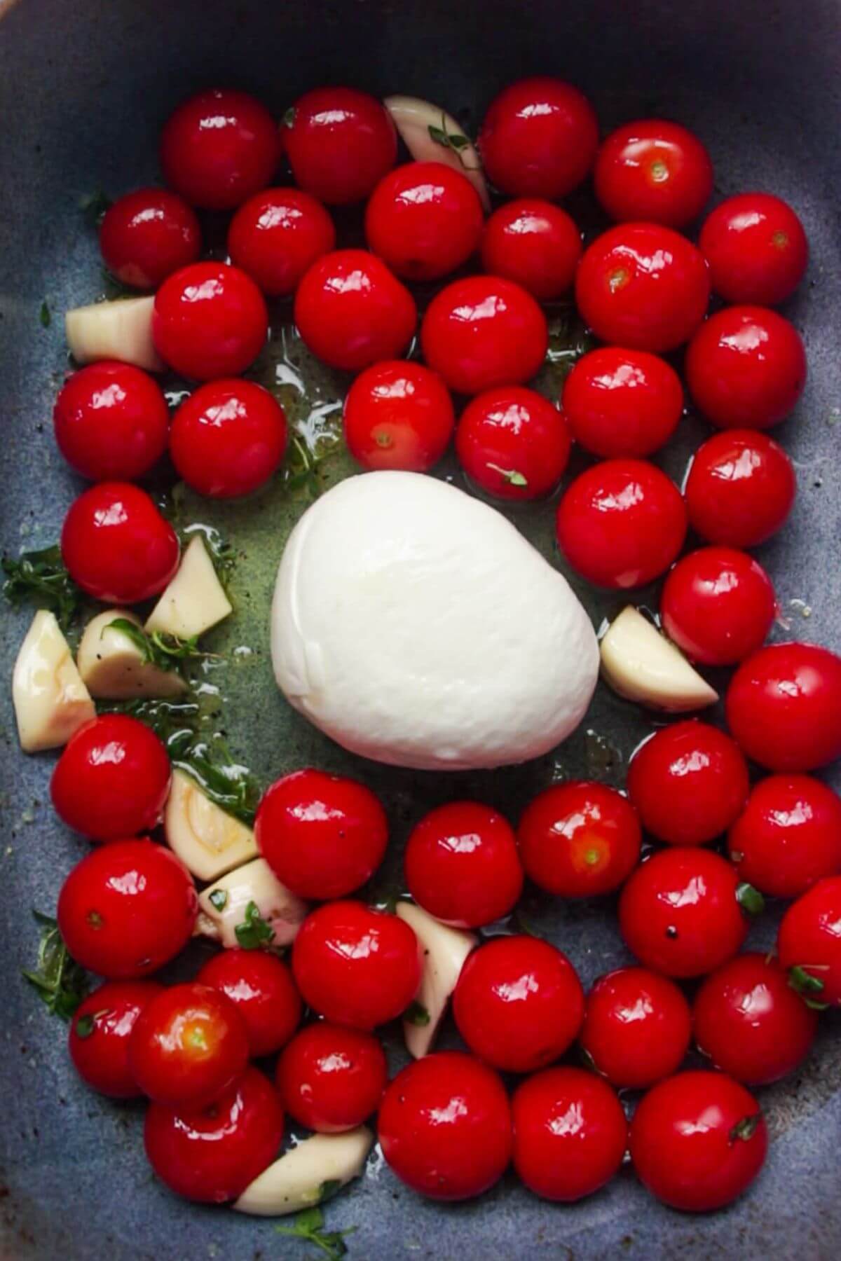 Burrata, cherry tomatoes, garlic, thyme and olive oil in a small blue oven dish.