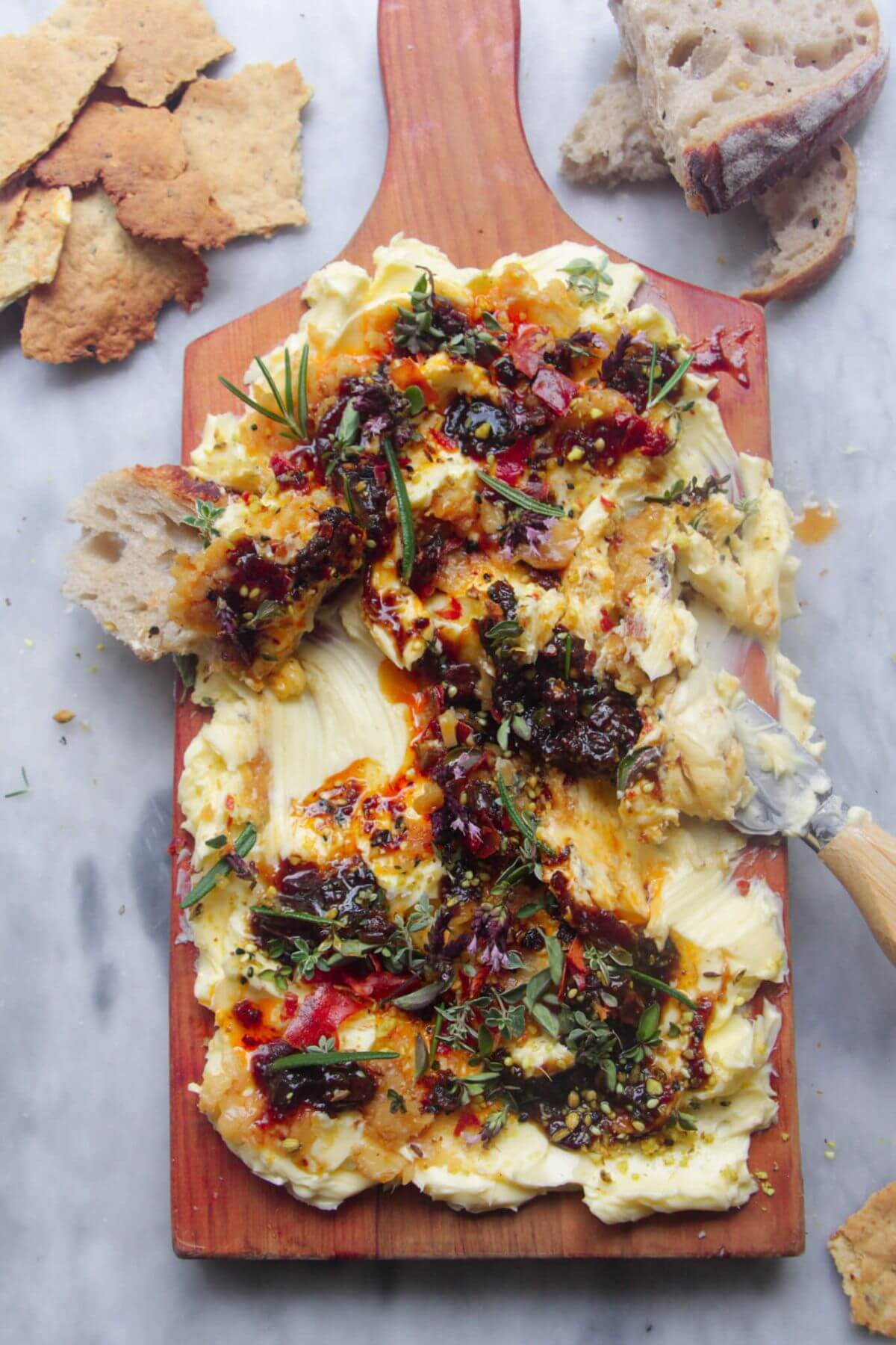 Butter smoothed onto a board and topped with chilli oil, fig chutney and herbs with bread on the side.