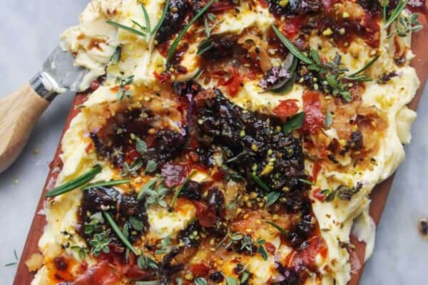 Butter smoothed onto a board and topped with chilli oil, fig chutney and herbs with crackers and bread on the side.