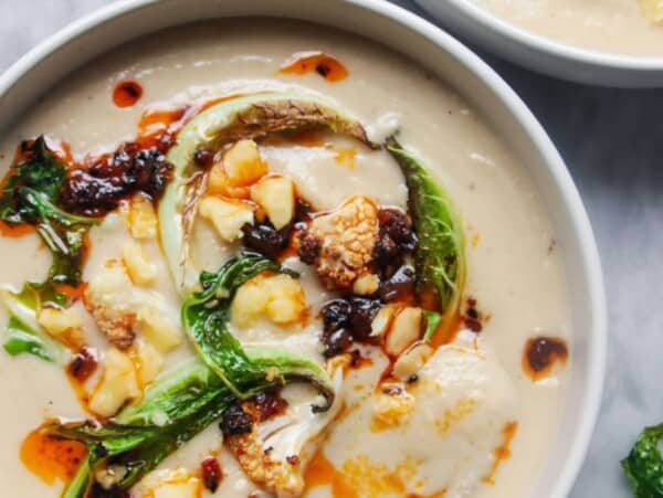 Close up of roasted cauliflower cheese soup in a bowl with another bowl just out of frame, on a grey marble background.