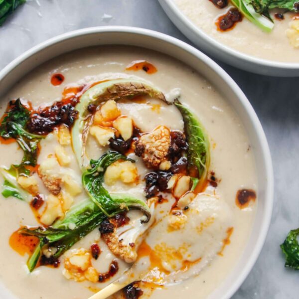 Close up of roasted cauliflower cheese soup in a bowl with another bowl just out of frame, on a grey marble background.