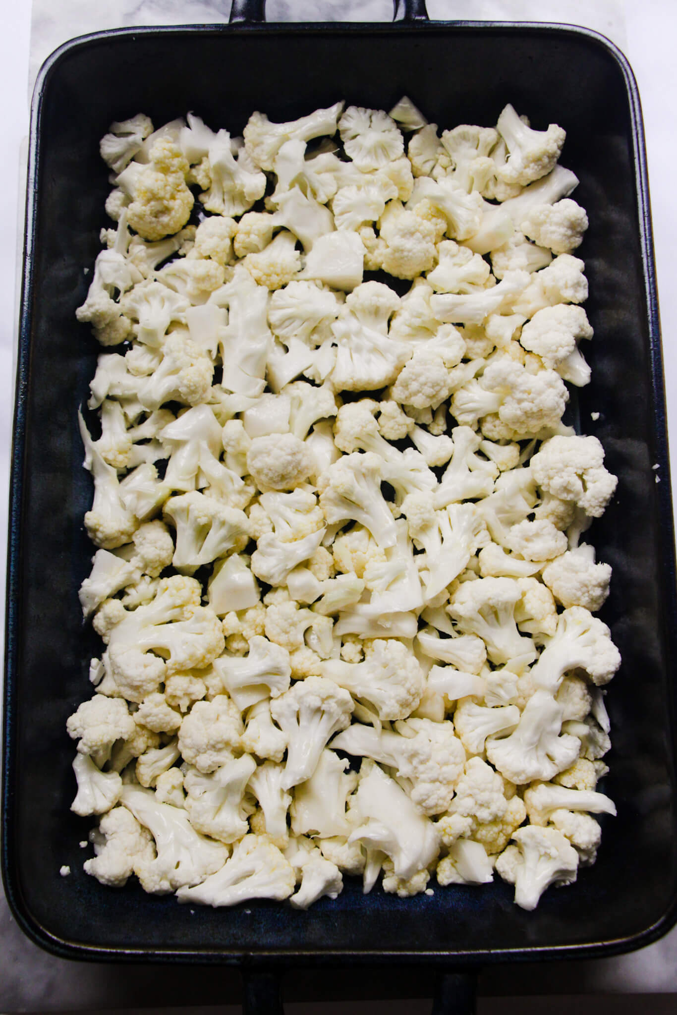 Cauliflower in a blue oven dish ready to be roasted.