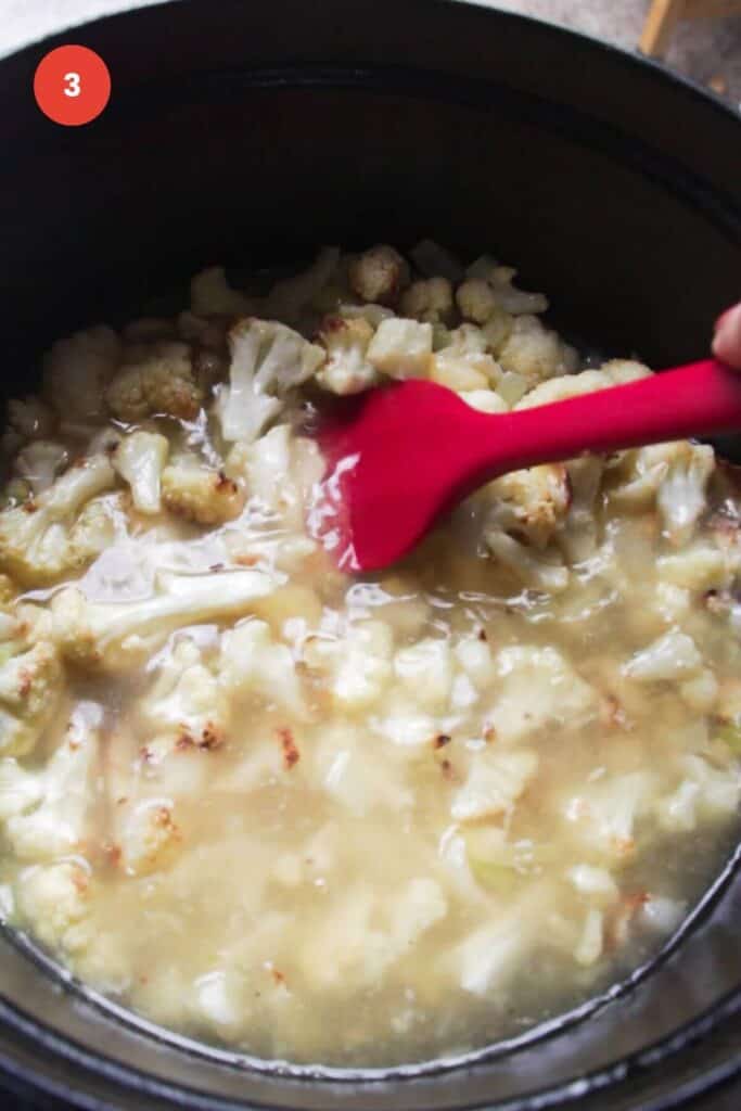 Stirring cauliflower florets in stock in a pot.