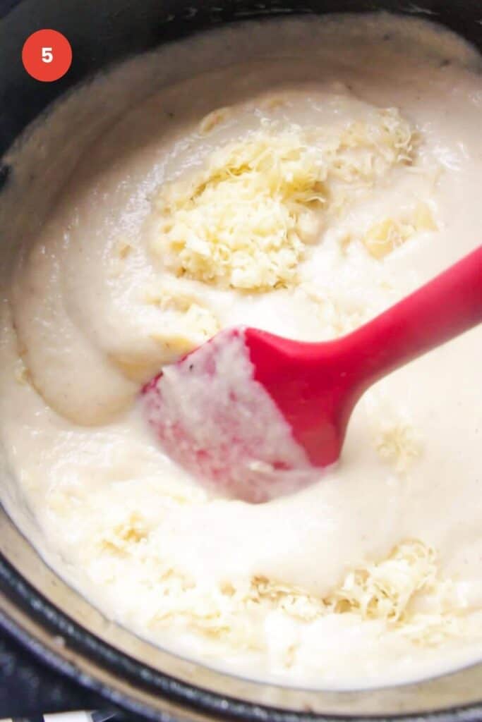 Blended cauliflower soup in a pot, stirring in grated cheese.