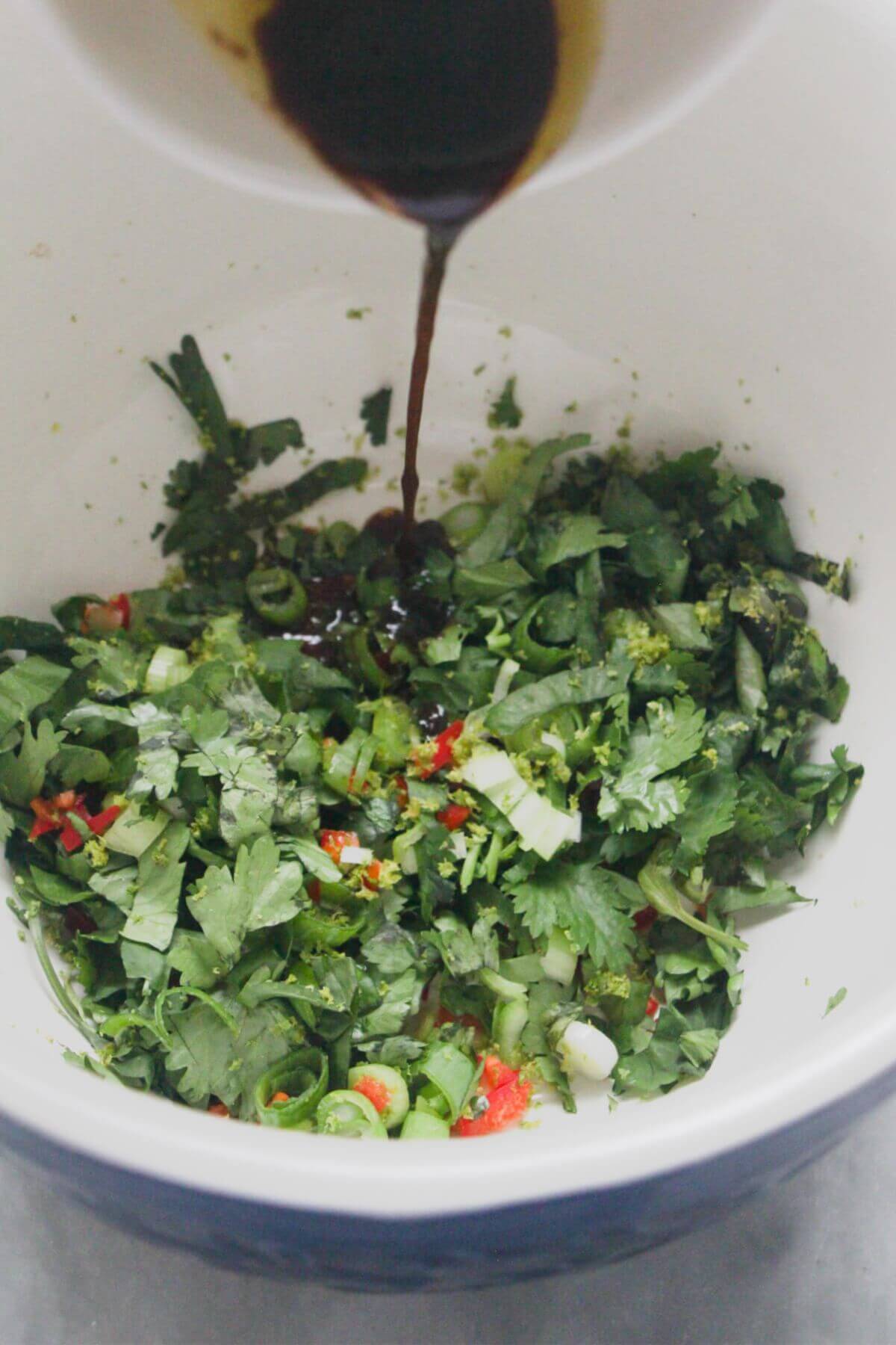 Lime juice and sesame oil being poured into a small bowl with coriander, chilli and spring onion.