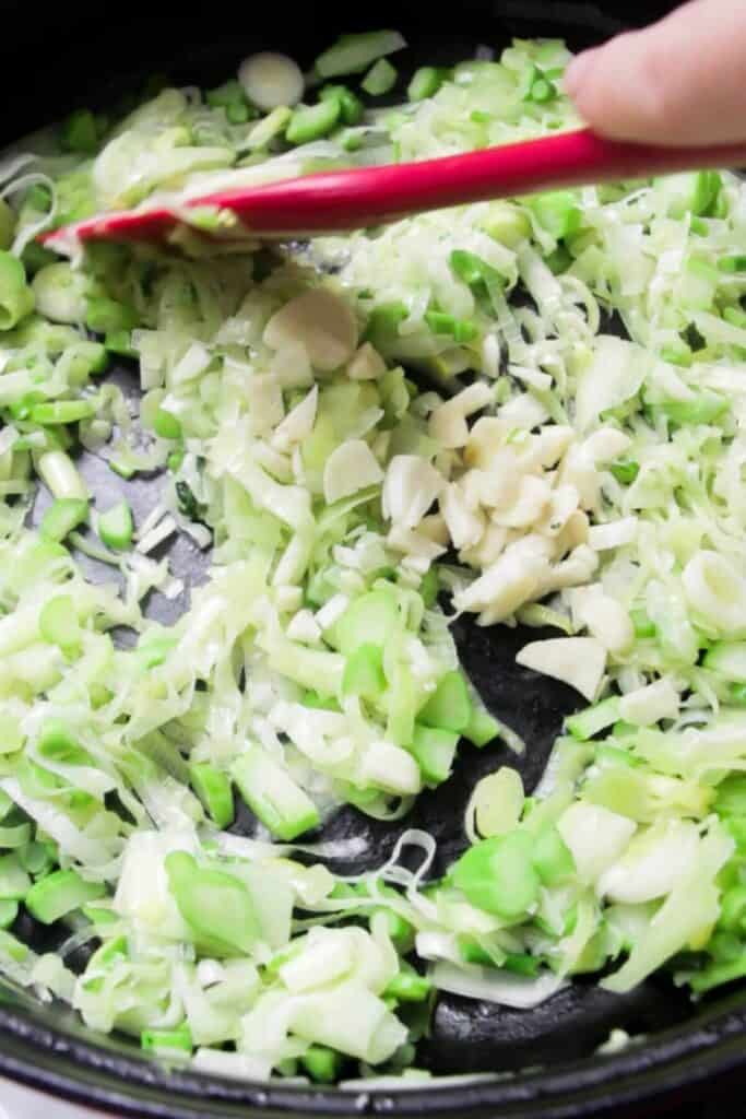 Red spatula stirring garlic, leeks and broccoli stems.