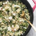 Creamy spinach and feta one pot orzo in a black and red pan on a grey marble background.