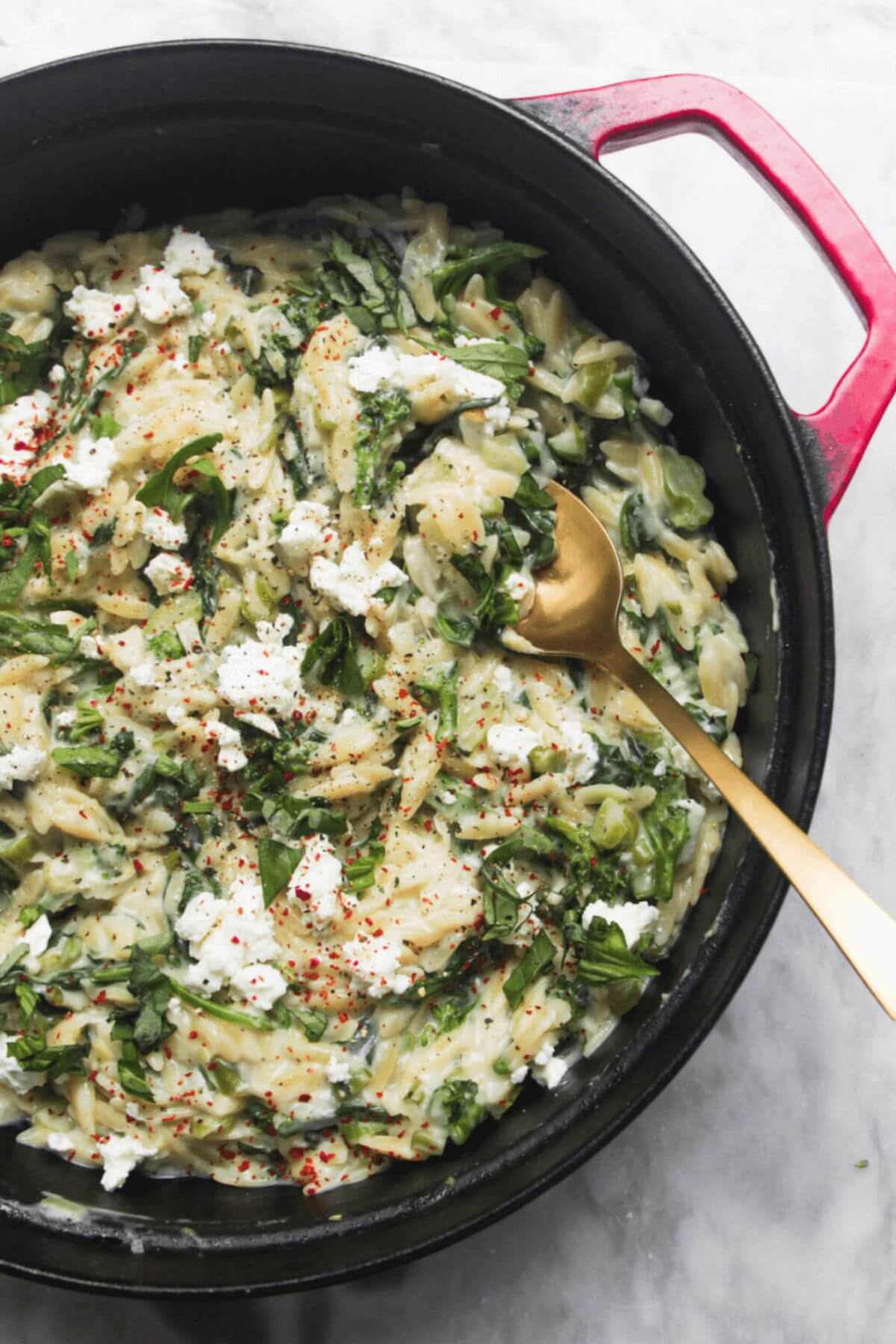 Creamy spinach and feta one pot orzo in a black and red pan on a grey marble background.