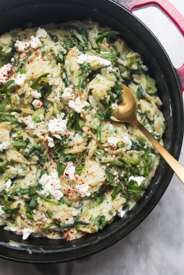 Creamy spinach and feta one pot orzo in a black and red pan on a grey marble background.