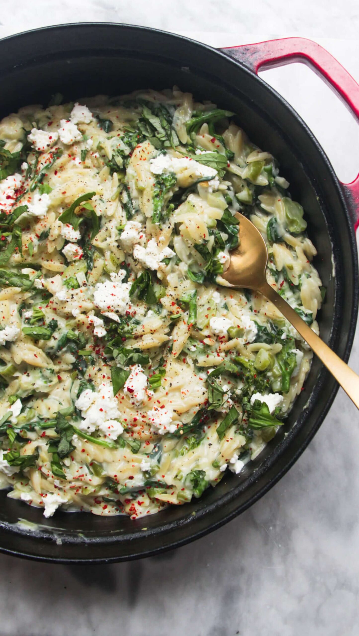 Creamy spinach and feta one pot orzo in a black and red pan on a grey marble background.
